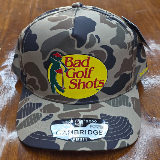 Camouflage golf ball case with 'Bad Golf Shots' logo on a wooden surface